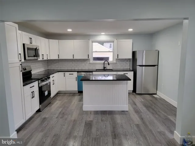 a kitchen with stainless steel appliances granite countertop a stove top oven a sink dishwasher and a refrigerator with wooden floor