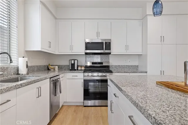 a kitchen with granite countertop a sink stainless steel appliances and white cabinets