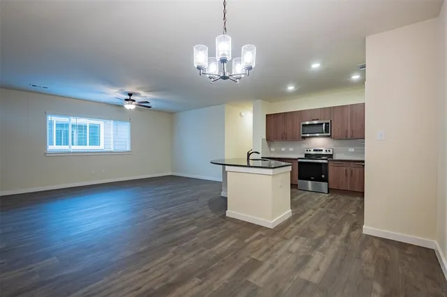 a kitchen with stainless steel appliances granite countertop a stove top oven a sink dishwasher a microwave oven and a dining table with wooden floor