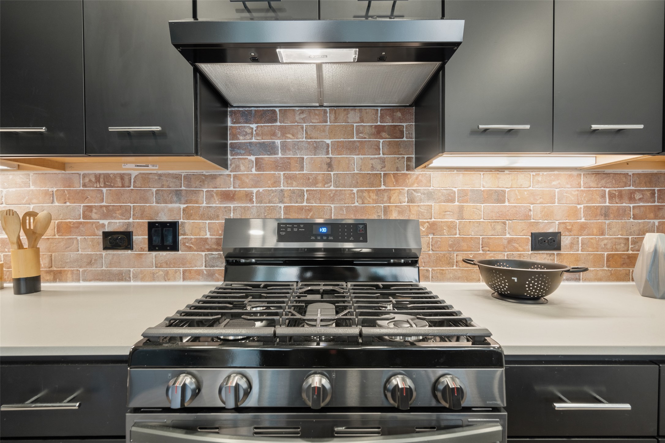 4510 Terry-O Lane, Unit 341 Austin, TX 78745 - Photo 10 of 40 Modern kitchen featuring dark cabinetry, a stainless steel gas range, and a brick-style backsplash