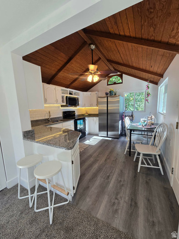 259 14th Street Ogden, UT 84404 - Photo 8 of 21 Kitchen featuring a vaulted wood-paneled ceiling with exposed beams, white cabinetry, a breakfast bar with a stone-finish countertop, stainless steel refrigerator, and wood-finish flooring