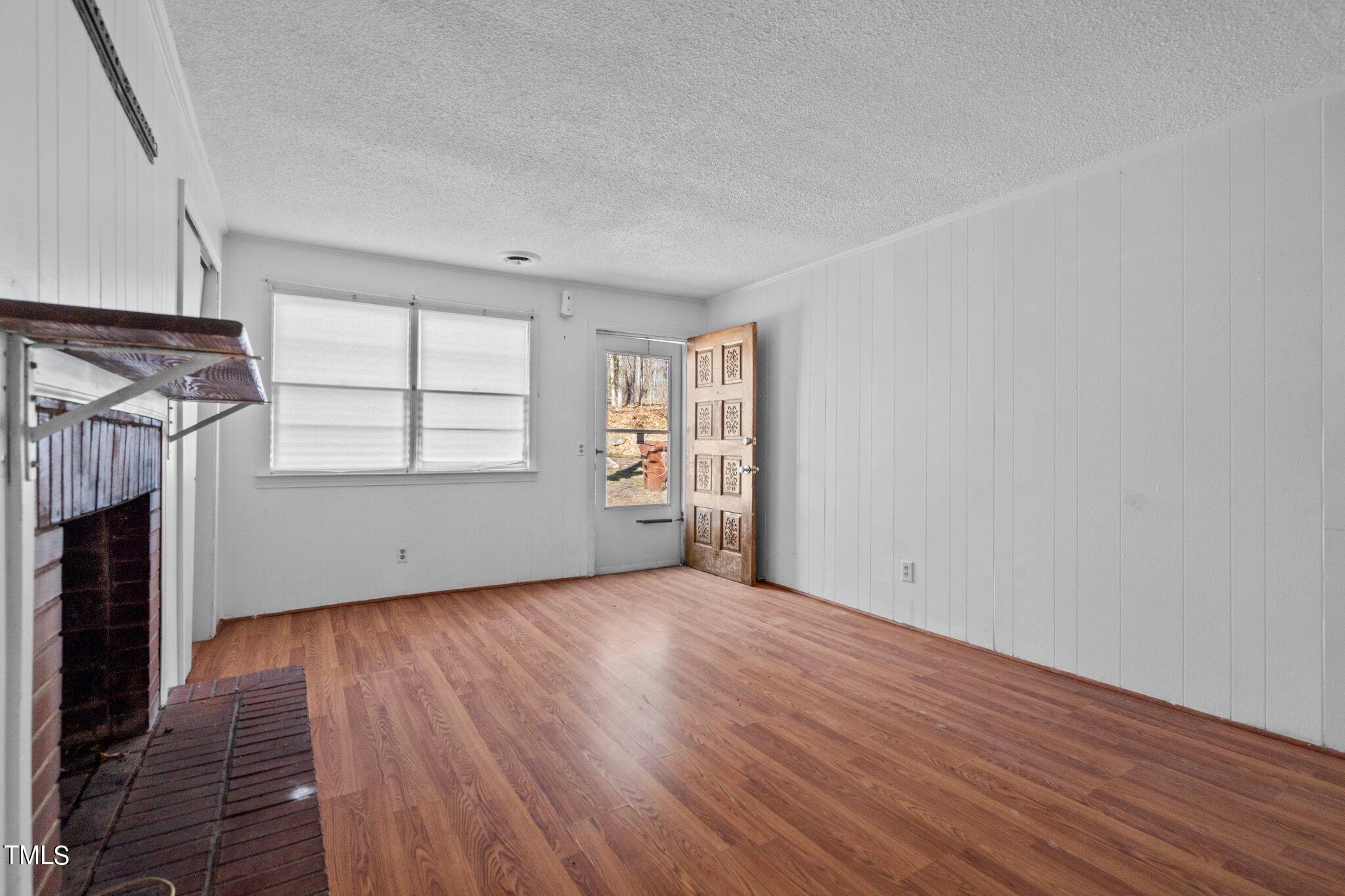 223 Gentry Street Roxboro, NC 27573 - Photo 6 of 36 an empty room with wooden floor fireplace and windows