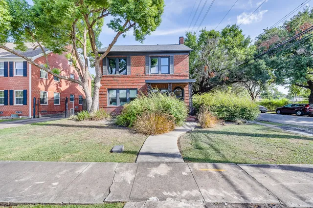 a view of a brick house with a yard plants and large tree