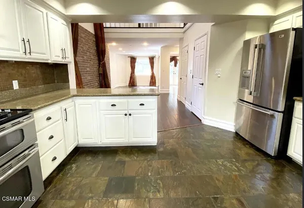 a kitchen with granite countertop a refrigerator a stove a sink and white cabinets