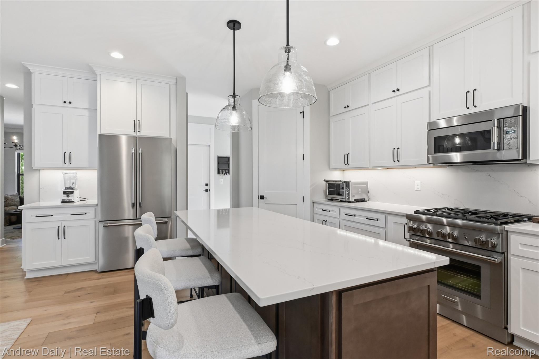 4661 Spears Road Pinckney, MI 48169 - Photo 24 of 56 Spacious kitchen featuring an oversized island with countertop seating, white shaker cabinetry, stainless steel appliances, and wood-finish flooring