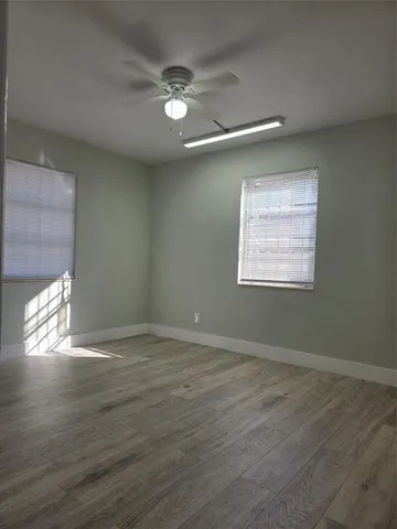 an empty room with wooden floor chandelier fan and windows