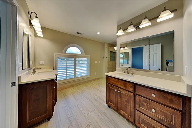 a spacious bathroom with a granite countertop double vanity sink a mirror and a shower
