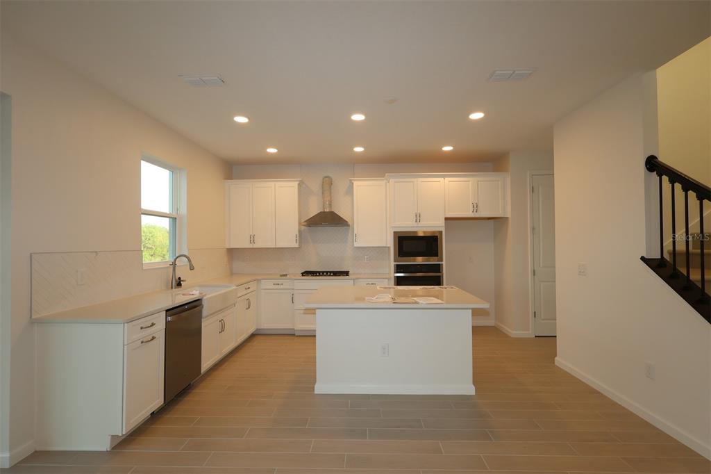 5426 Park Guell Street St. Cloud, FL 34771 - Photo 7 of 64 a kitchen with stainless steel appliances kitchen island granite countertop a refrigerator a sink dishwasher a stove and a refrigerator with wooden floor