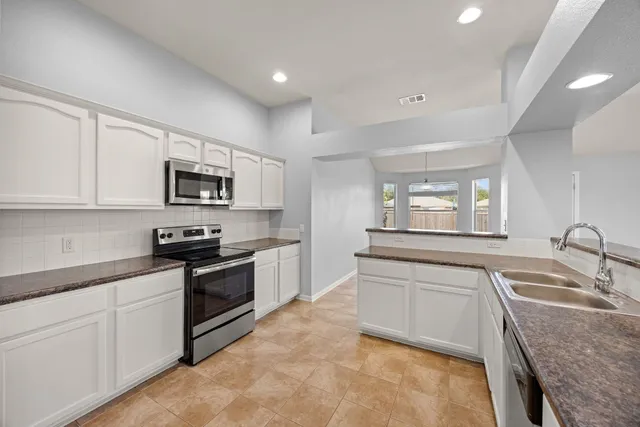 a kitchen with granite countertop a sink white cabinets and stainless steel appliances