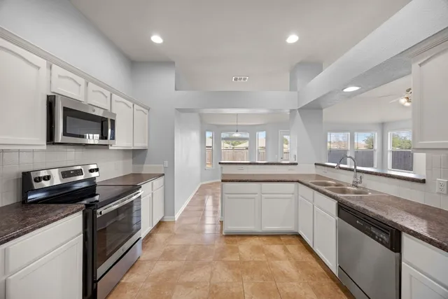 a large kitchen with stainless steel appliances granite countertop a sink dishwasher stove top oven and wooden cabinets
