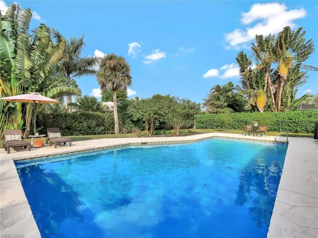 a view of pool with lawn chairs under an umbrella