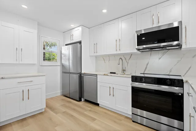 a kitchen with stainless steel appliances kitchen island granite countertop a dining table chairs and white cabinets