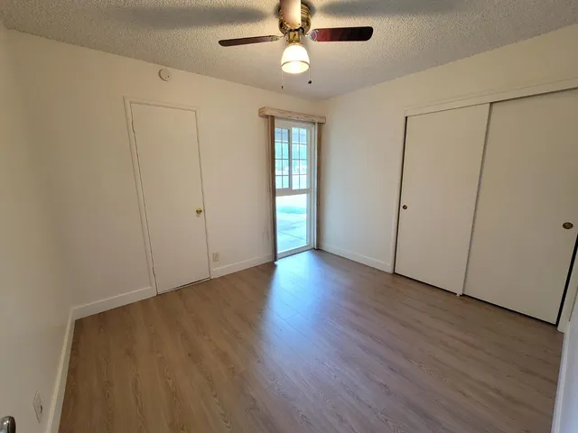 an empty room with wooden floor fan and windows