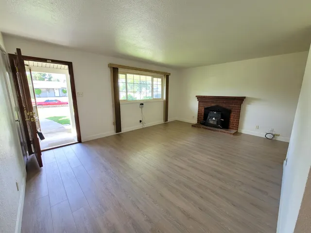 an empty room with wooden floor fireplace and windows