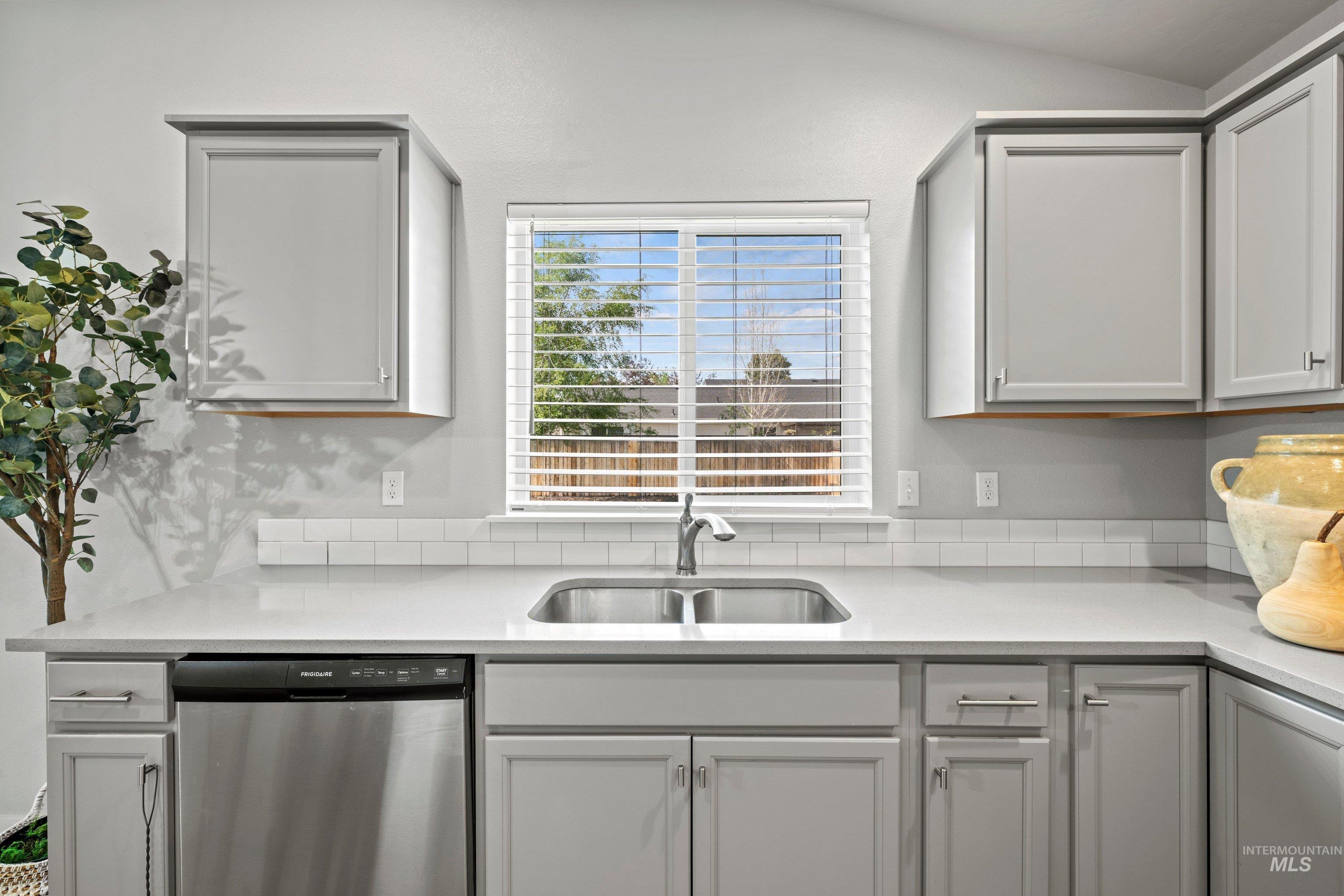 12744 West Fig Street Boise, ID 83713 - Photo 16 of 34 Kitchen featuring light gray cabinetry with brushed nickel hardware, a stainless steel double-basin sink with a gooseneck faucet, light-toned countertops, and a white subway tile backsplash