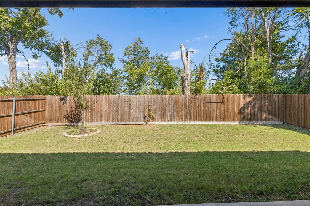 5224 Troupe Road McKinney, TX 75071 - Photo 25 of 31 Fenced backyard with a grassy lawn, mature perimeter trees, and a young tree with stone-edged landscaping