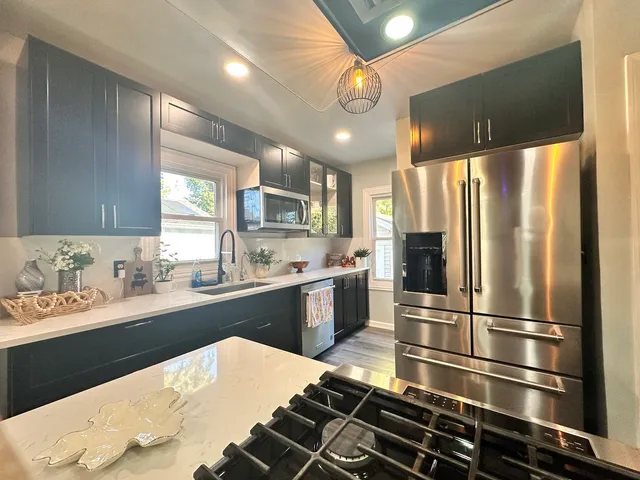 a kitchen with stainless steel appliances kitchen island granite countertop a refrigerator a sink dishwasher a stove and white cabinets with wooden floor