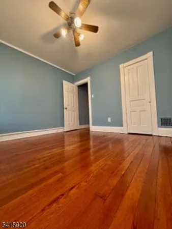an empty room with wooden floor chandelier fan and windows