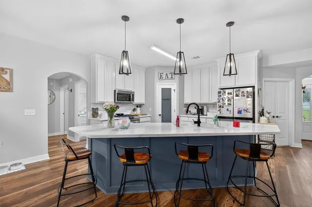 a open kitchen with stainless steel appliances granite countertop a sink dishwasher a stove a refrigerator and a dining table with wooden floor