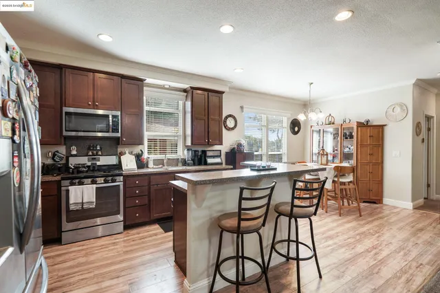 a kitchen with stainless steel appliances kitchen island granite countertop a refrigerator a stove top oven and a dining table with wooden floor