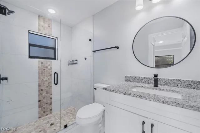 a bathroom with a granite countertop sink a mirror a toilet and shower