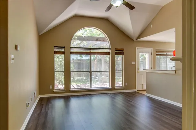 an empty room with wooden floor fan and windows