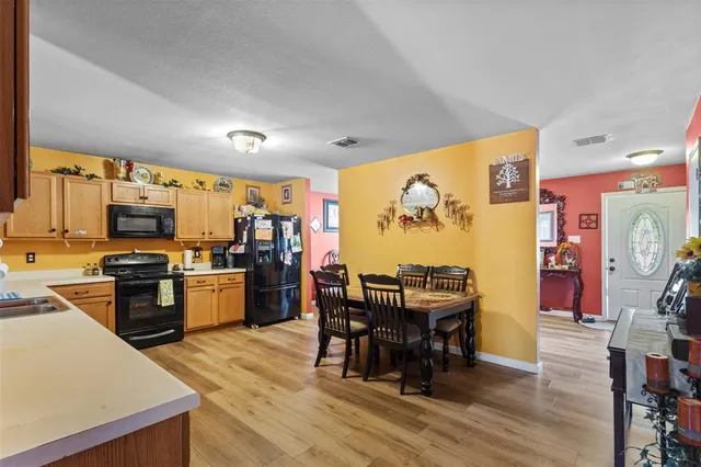 a kitchen with stainless steel appliances kitchen island granite countertop a refrigerator a stove top oven a dining table and chairs with wooden floor