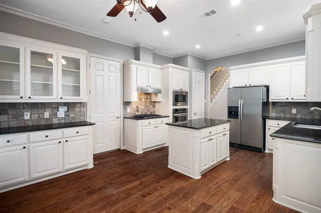 a kitchen with granite countertop a refrigerator a stove a sink cabinets and wooden floor