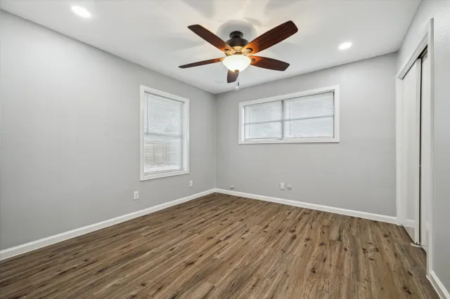 an empty room with wooden floor ceiling fan and windows