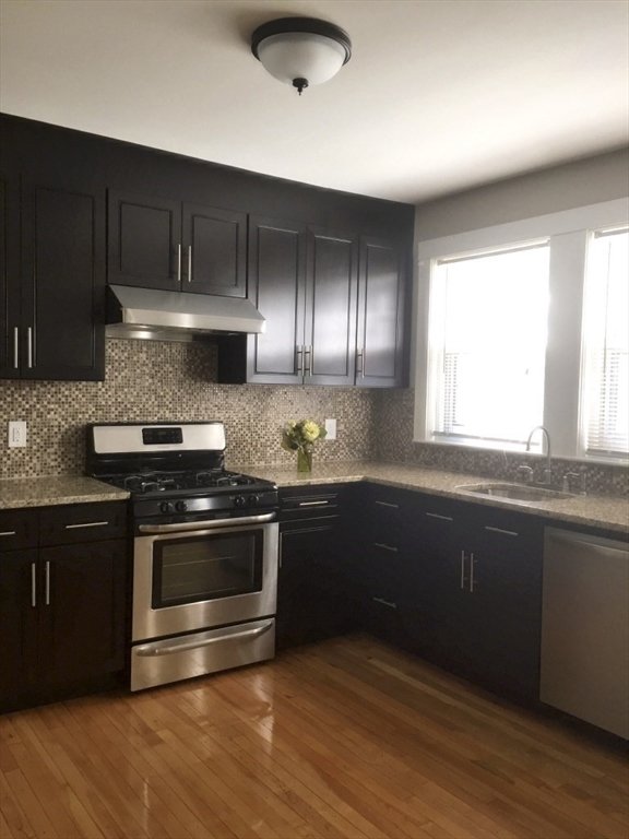 90 Orchard Street, Unit 1 Boston, MA 02130 - Photo 6 of 10 a kitchen with granite countertop wooden cabinets stainless steel appliances and a window