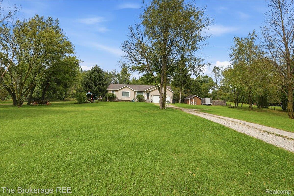 11282 Silver Lake Road Byron, MI 48418 - Photo 22 of 32 Expansive green lawn, gravel driveway, detached shed, mature trees, and single-story residence