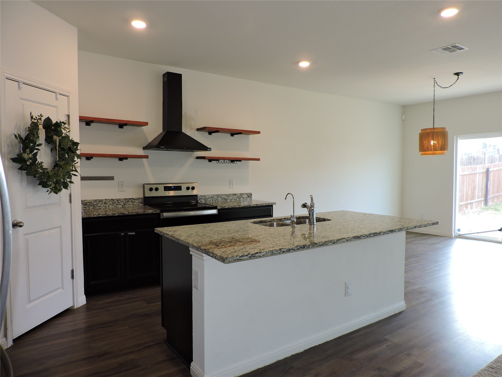 14120 Jeannette Rankin Rd Manor Manor, TX 78653 - Photo 3 of 25 Kitchen with light stone counters, dark wood-style floors, hanging light fixtures, and a center island with sink