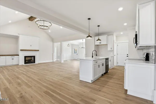 a large kitchen with granite countertop a white stove top oven and white cabinets with wooden floor