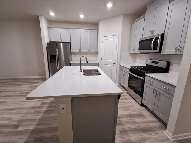 a kitchen with kitchen island granite countertop a sink a stove top oven a refrigerator cabinets and wooden floor