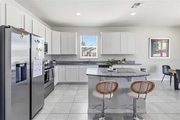 a kitchen with stainless steel appliances granite countertop a stove a sink a refrigerator and chairs