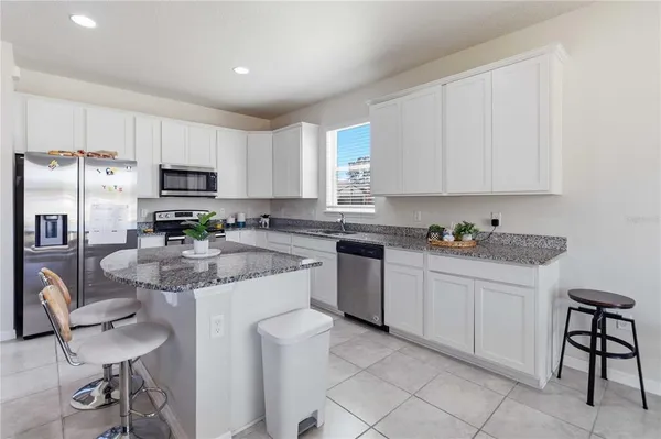 a kitchen with stainless steel appliances granite countertop a stove a sink a microwave a refrigerator and white cabinets