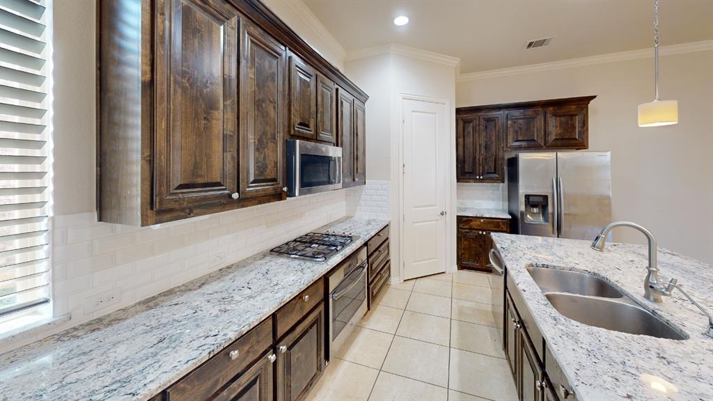 14712 Spitfire Trail Fort Worth, TX 76262 - Photo 7 of 25 Gourmet kitchen featuring dark wood cabinetry, light granite countertops, a subway tile backsplash, stainless steel appliances, and a central island with a double basin sink