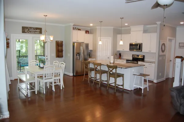 a kitchen with stainless steel appliances kitchen island granite countertop a refrigerator a stove a dining table and chairs with wooden floor