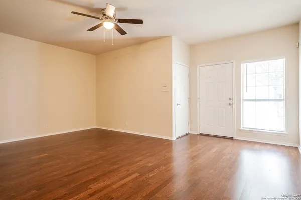 an empty room with wooden floor ceiling fan and windows