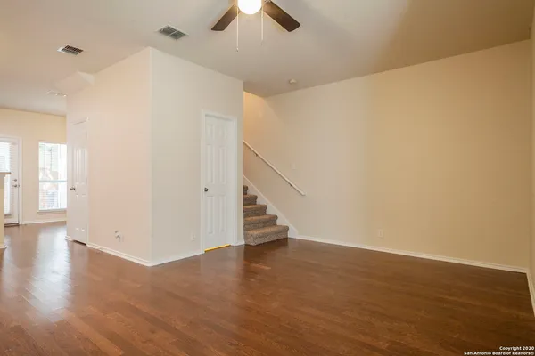 a view of an empty room with wooden floor and a ceiling fan