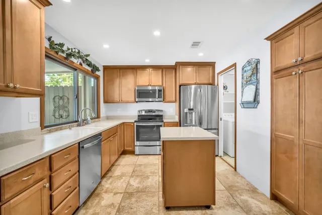 a kitchen with stainless steel appliances granite countertop a refrigerator a sink dishwasher a oven and a dining table with wooden cabinet