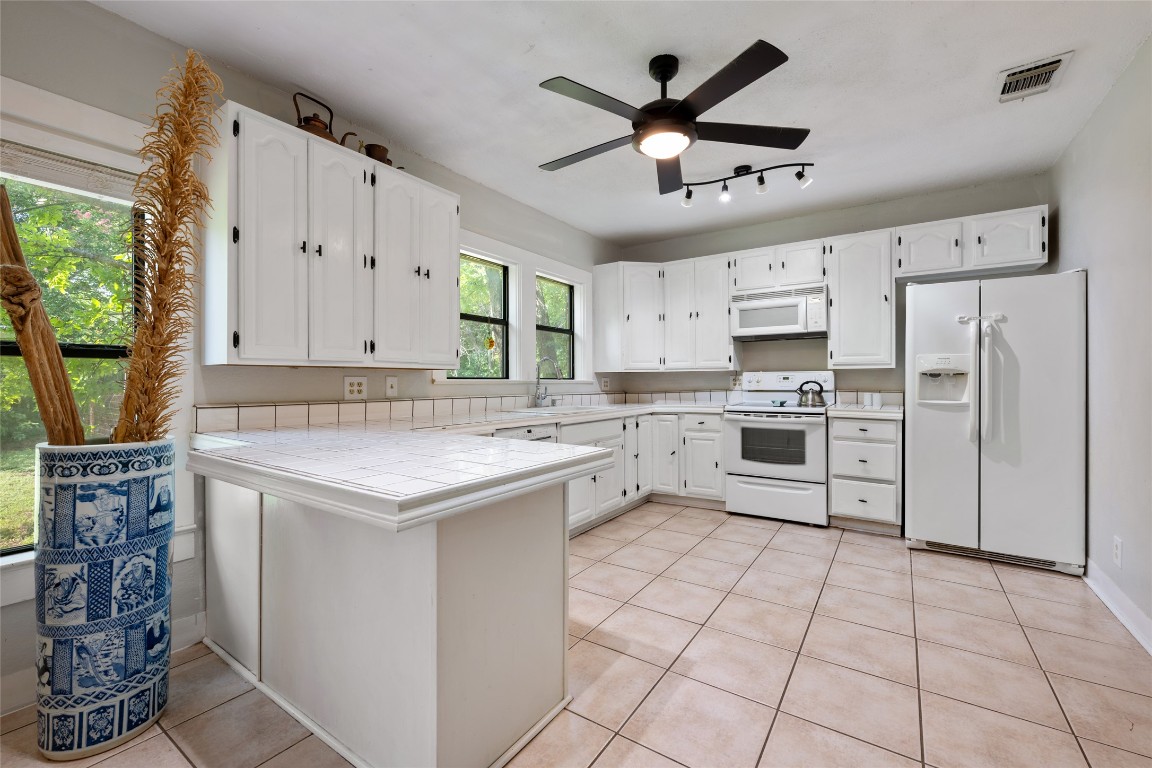 555 Hopewell Road Bertram, TX 78605 - Photo 11 of 21 Kitchen with tile countertops, white appliances, white cabinetry, light tile patterned floors, and a peninsula