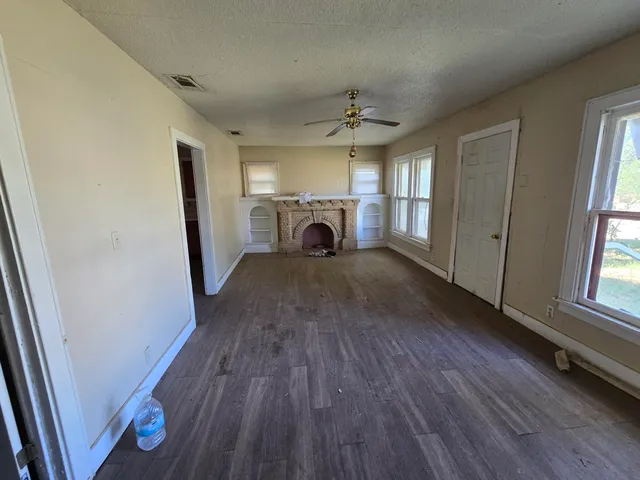 an empty room with wooden floor fireplace and windows