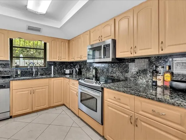 a kitchen with granite countertop white cabinets a sink a window and stainless steel appliances