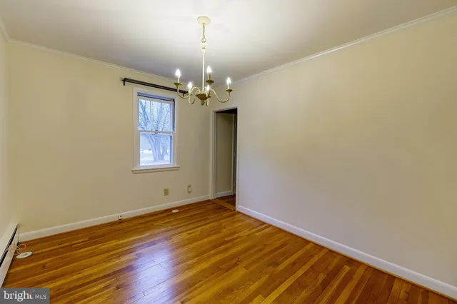 an empty room with wooden floor chandelier and windows