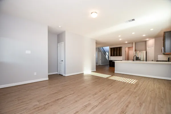 an empty room with wooden floor and kitchen view