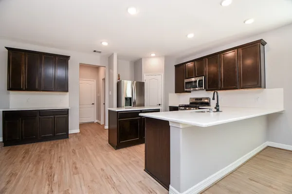 a kitchen with stainless steel appliances a stove top oven a sink dishwasher a refrigerator and a oven with wooden floor