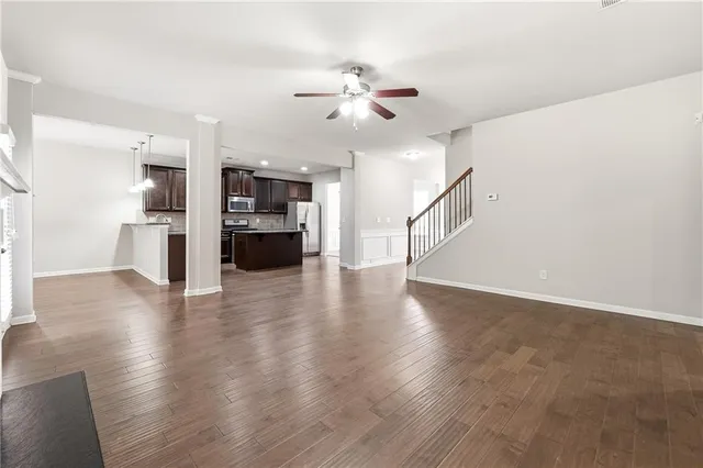 a view of an empty room with wooden floor and a ceiling fan