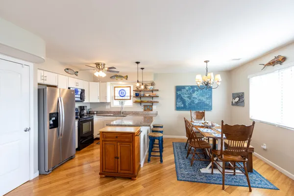 a kitchen with stainless steel appliances kitchen island granite countertop a refrigerator a stove top oven a dining table and chairs with wooden floor
