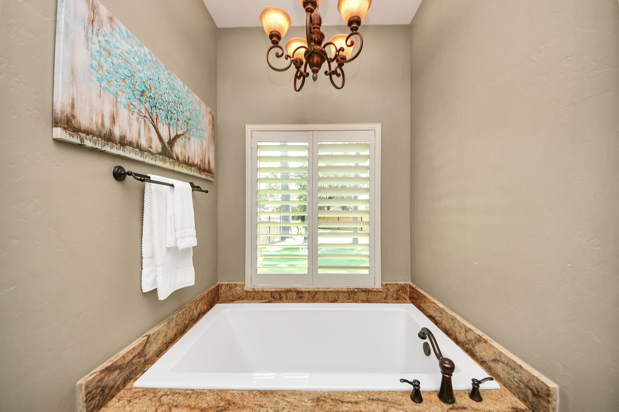702 Fairway Oaks Conroe, TX 77302 - Photo 25 of 42 This bathroom features a
luxurious soaking tub with
elegant marble surrounds and
bronze fixtures. It has a large
window with plantation shutters
providing natural light,
complemented by a stylish
chandelier and tasteful wall art.